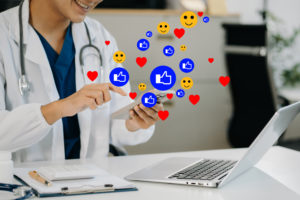 Marketing médico: torne-se referência no mercado 1 Médico usando seu celular em consultório com vários ícones de curtidas e emojis ao seu redor