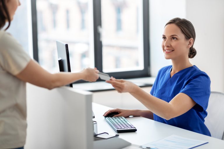 Médica sorridente entregando cartão de seguro ou crédito a paciente em ambiente hospitalar