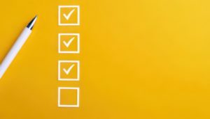 Caneta ao lado de um checklist com três itens preenchidos e um vazio em fundo amarelo