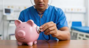 Médico usando um estetoscópio para escutar o interior de um cofre de porquinho rosa