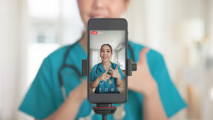 Médica de jaleco verde usando um celular para gravar uma live