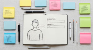 Caderno ao centro com ilustração de uma persona com seus dados ao lado, rodeado por post-its coloridos