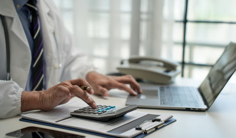 Médico usando computador e calculadora para analisar o faturamento de convênios