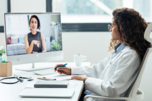 Médica realizando um atendimento à distância em seu consultório usando um computador