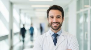 Médico de jaleco branco ao centro com corredor desfocado ao fundo