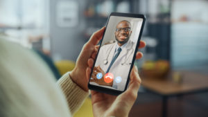 Paciente segurando um celular com a imagem de um médico em teleatendimento