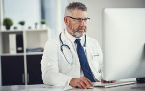 Médico sentado em frente a um computador usando um sistema para consultório