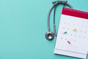 Calendário com alguns lembretes presos sobre ele logo a frente de um estetoscópio em fundo azul