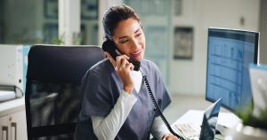 Médica sorridente atendendo ligação telefônica em ambiente hospitalar, representando atendimento e organização na clínica