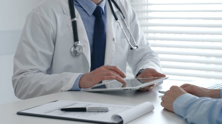 Profissional de saúde mostrando informações em tablet para paciente durante consulta, representando comunicação clara no atendimento