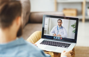 Homem sentado em sofá de costas assistindo um webinar para paciente em notebook
