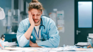 Médico com a mão na cabeça em hospital demonstrando frustração