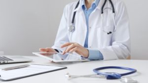 Médica sentada em mesa usando um tablet para fazer prescrição médica digital