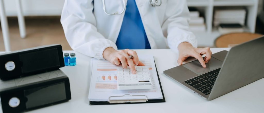Médico utilizando calculadora e tablet para analisar custos e indicadores financeiros em ambiente hospitalar