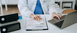 Médico utilizando calculadora e tablet para analisar custos e indicadores financeiros em ambiente hospitalar