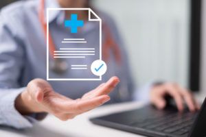 Como anexar arquivos no prontuário eletrônico Afya iClinic 1 Médico em frente a notebook com uma imagem holográfica sobre a sua de um arquivo sendo anexado