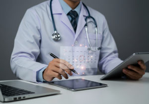 Médico de jaleco branco e estetoscópio usando dois tablets e um notebook para otimizar agenda
