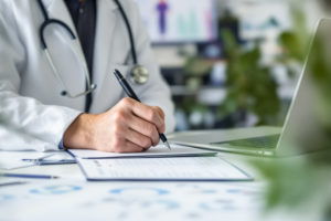 Médico de jaleco branco escrevendo em papel e configurando agenda médica personalizável no computador
