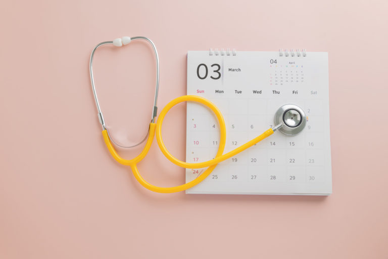 Estetoscópio amarelo com a sua ponta marcando uma data em um calendário em fundo rosa